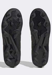 Suela de zapatilla deportiva negra con clavos de tracción distintos, diseño curvado, superficie texturizada y logotipo del fabricante visible en el área del talón.