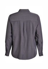 Aizmugures skats uz pelēku krekli ar garām piedurknēm, kas ir ar plisējumu zem jostas, pogu aprocēm un klasisku apkakli.