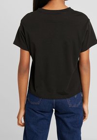 Czarny bawełniany t-shirt o luźnym kroju, z krótkimi rękawami i prostym dołem. Noszony z niebieskimi dżinsami, podkreślając swobodny styl.