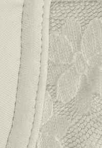 Vitt tyg med en texturerad spetssektion med blommönster, åtskild av en slät, bomullsliknande vit kant.