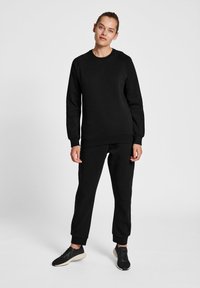 Zwart trui en bijpassende joggers hebben een eenvoudig ontwerp en een zachte textuur, aangevuld met zwarte sportschoenen.