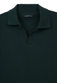 Polo verde scuro con un motivo a nido d'ape testurizzato, colletto corto e design a scollo a V; etichetta visibile che indica la taglia L.