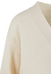 Kremowy sweter dzianinowy z dekoltem w serek i subtelnymi detalami teksturowymi wzdłuż kołnierza i szwów ramion.