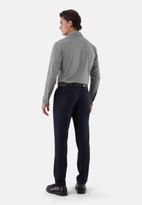 Camicia a maniche lunghe a righe in grigio e bianco, abbinata a pantaloni blu navy. Scarpe nere con finitura in pelle liscia. Nessun motivo visibile sui pantaloni.