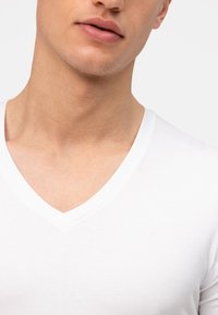 Witte katoenen V-hals t-shirt met een gladde textuur, strakke pasvorm en een nette halslijn. Er zijn geen patronen of extra accenten zichtbaar.