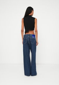 Μαύρο cropped αμάνικο τοπ με στρογγυλεμένο λαιμό και ξέφτια στο τελείωμα, συνδυασμένο με τζιν παντελόνι φαρδιάς γραμμής με ψηλή μέση και μπλε ταμπελάκι.