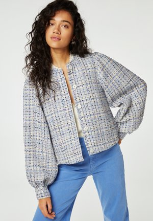 Tweed jasje in wit en blauw, met een gestructureerd patroon, ronde halslijn, knoopsluiting en ballonmouwen. Gecombineerd met blauwe broek.