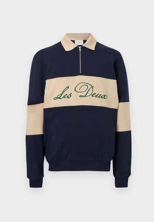 Dlouhý rukáv modro-námořnický a béžový pulovr s půlzipem u límce a výšivkou "Les Deux" zeleně na béžovém panelu na hrudi.
