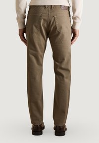 Pantalones de algodón marrón con un corte recto, que cuentan con dos bolsillos traseros y un detalle de diseño cosido, combinados con zapatos oscuros.