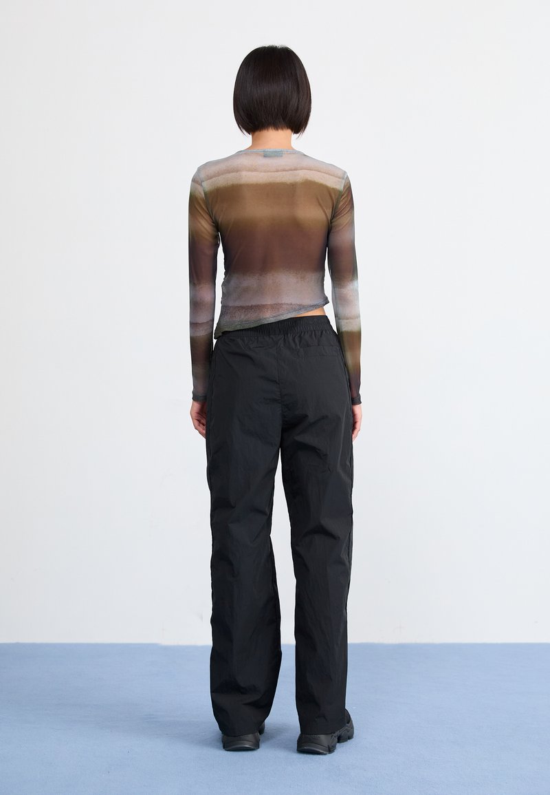 Haut à manches longues dans un dégradé de marrons et de bleus avec un design ajusté, associé à un pantalon noir ample et des chaussures noires.