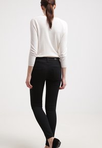 Černé úzké džíny s středním pasem, se zadními kapsami a hladkým povrchem. V kombinaci se světle bílým topem s dlouhým rukávem.