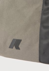 Κοντινή ματιά σε μπεζ ύφασμα με μαύρη υφή κάθετης ρίγας και μικρό μαύρο γεωμετρικό λογότυπο κοντά στην κάτω αριστερή γωνία.