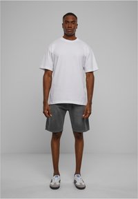 Camiseta blanca de algodón con mangas cortas, combinada con pantalones cortos de denim gris oscuro. El modelo lleva zapatillas gris y blancas con rayas negras.