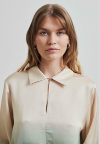 Blusa di raso con effetto ombré in beige pallido e verde, caratterizzata da un colletto a punta, piccola chiusura con bottoni e maniche lunghe.