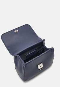 Námořnická kožená taška se stříbrným zámkem, otevřená tak, aby odhalila prostorný interiér s tmavým podšíváním a malou etiketou viditelnou uvnitř.