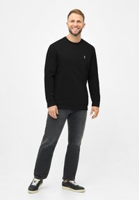 Sudadera negra con cuello redondo y mangas largas, combinada con jeans oscuros y zapatillas negras con cordones blancos. Diseño simple.