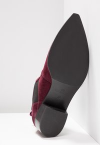 Burgundy suede shoe with a textured black panel and a solid black heel. Stamped logo and size "37" visible on the heel's side.