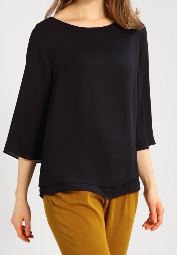 Blouse noire légère avec un col bateau et des manches cloche trois-quarts ; le tissu semble lisse avec un drapé fluide. Associée à un pantalon moutarde.