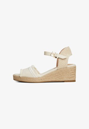 Platform wedge sandal with a textured cream upper, contrasting white stripes, ankle strap with gold hardware, and woven jute detailing.