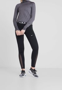 Leggings de sport noirs avec des panneaux en mesh, associés à un haut gris ajusté à manches longues. Des chaussures de course noires et grises complètent la tenue.