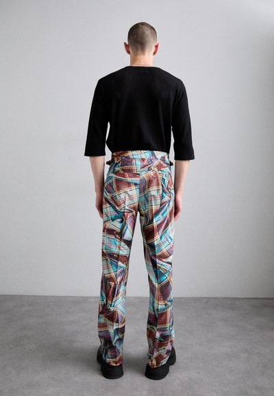 Schwarzes Netzshirt und bunte Karohosen mit kantigen Mustern und Seitentaschen, kombiniert mit schwarzen klobigen Schuhen.