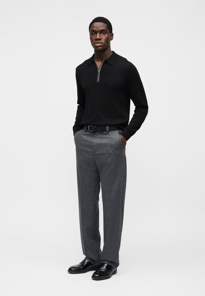 Μαύρο πόλο με μακριά μανίκια και φερμουάρ στον γιακά, σε συνδυασμό με γκρι παντελόνι με ρίγες και μαύρα παπούτσια. Απλός, ραμμένος εκλεπτυσμένα και με λεία υφή.