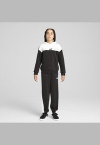 Chándal PUMA en blanco y negro que incluye una sudadera con capucha y un bolsillo canguro, así como pantalones jogger con franjas laterales blancas. Zapatillas negras.