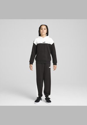 Chándal PUMA en blanco y negro que incluye una sudadera con capucha y un bolsillo canguro, así como pantalones jogger con franjas laterales blancas. Zapatillas negras.