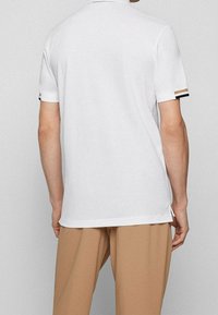 Chemise polo blanche au design classique, dotée de manches courtes avec des accents rayés et de fentes latérales à l'ourlet.