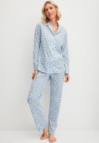 Lichtblauw pyjamastel met een bloemenpatroon en geometrische vormen. De top heeft een kraag en knopen, en de broek heeft een recht model.