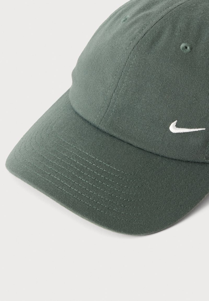 Grøn baseballcap med buet skygge og lille hvid Nike swoosh-logo på forsiden mod en ensfarvet baggrund.
