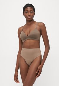 Woman wearing matching beige seamless bra and high-waisted underwear, standing against a plain white background.