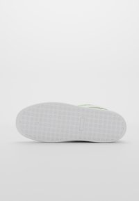 Semelle de chaussure en caoutchouc blanc avec motifs de petits losanges et points, photographiée par dessous sur un fond blanc.