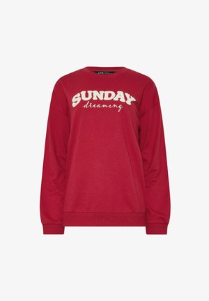 Punainen pitkähihaisia huppari, jossa edessä valkoiset tekstuurilla kirjaillut sanat "SUNDAY dreaming". Pehmeää, rentoa kangasta.