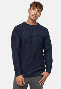 Mørkeblå strikket sweater med et tekstureret mønster, rund halsudskæring og ribbede mansjetter og kant. Materialet ser blødt og varmt ud.