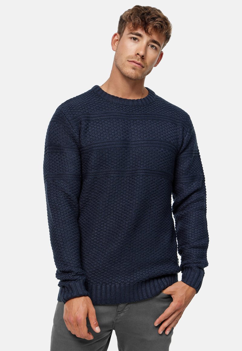 Mørkeblå strikket sweater med et tekstureret mønster, rund halsudskæring og ribbede mansjetter og kant. Materialet ser blødt og varmt ud.