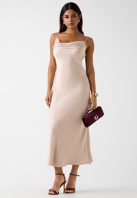Długa, bezrękawnikowa sukienka z beżowego satynu z delikatnie drapowanym dekoltem i subtelnym wzorem w kropki, zestawiona z głęboką bordową kopertówką i sandałkami na paski.