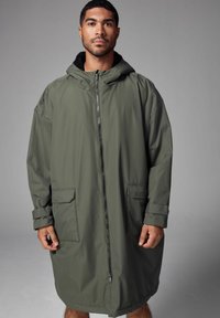 Olivgrüne wasserdichte Jacke mit Kapuze, Reissverschlüssen und zwei vorderen Taschen. Sie hat einen lässigen Schnitt und ein weiches, strukturiertes Innenfutter.