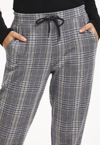Grå och marinblå rutiga byxor med resårmidja och dragsnöre, som har sidofickor och ett mjukt texturerat tyg.