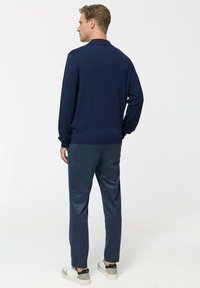 Polo-shirt navy cu mânecă lungă, material texturat, guler ribat. Asortat cu pantaloni tapered de culoare albastru deschis și adidași gri cu accente negre.