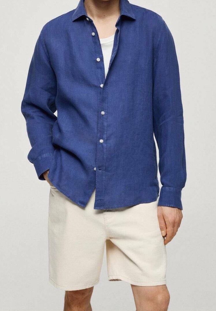 Chemise en lin bleue à boutons, manches longues, texture de tissu légère et boutons blancs, associée à un short de couleur crème.