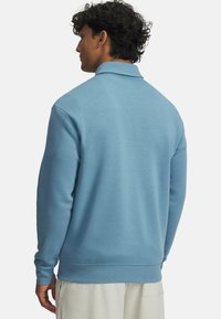 Svetlo modra pulover jopica s ovratnikom, dolgimi rokavi in rebrastim robom. Gladka tekstura, preprost dizajn, oblečena z belimi teksturiranimi kratkimi hlačami.