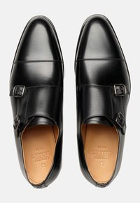 Schwarze Lederschuhe mit einer glatten Oberfläche, ausgestattet mit zwei Schnallen im Mittelfußbereich und einem spitzen Zehen-Design. Helle beige Innenauskleidung.