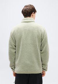 Ανοιχτό πράσινο φλις μπουφάν με ψηλό γιακά, με μαλακή, υφή εξωτερική επιφάνεια. Μακριά μανίκια και άνετη εφαρμογή με ίσια ζώνη στη μέση.