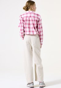 Camisa de franela a cuadros en rosa y blanco con la parte trasera recogida, combinada con pantalones de pierna ancha en beige claro y zapatillas deportivas plateadas.