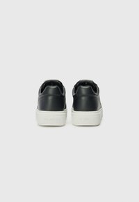 Zwarte leren sneakers met een witte rubberen zool, ronde neus en contrasterende hakdetail, met verhoogde merktekst op de achterkant.