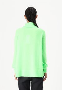 Neon grønn oversized genser med høy krage, ribbestrikkede mansjetter og hem. Teksturert stoff med droppet skulderdesign.