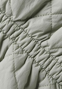 Tissu matelassé d'une teinte verte douce avec des coutures diagonales et une texture plissée, présentant un matériau lisse et un éclat subtil.