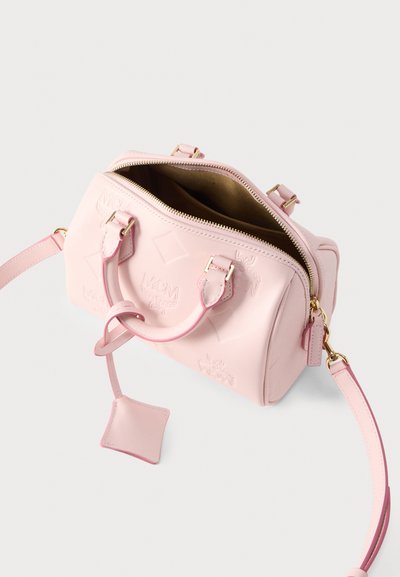 Ροζ δερμάτινη τσάντα χειρός με ανάγλυφο λογότυπο, χρυσλό φερμουάρ, κοντές λαβές και μακρύ ρυθμιζόμενο ιμάντα ώμου, ανοιχτή για να φαίνεται η εσωτερική επένδυση.