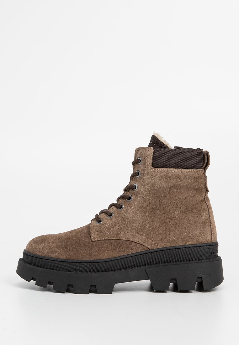 Bottines en suède marron avec une épaisse semelle en caoutchouc noir, bout rond et œillets en métal. Doublées d'un matériau doux en haut.